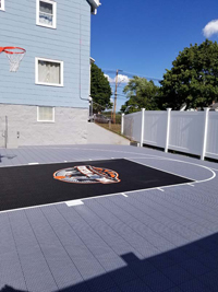 View from other side of most of Boston, MA titanium and black home basketball court surface featuring unique Hoop Head logo. This shows use of space right up against the house, working around uneven protrusions.
