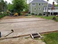 Site work preparing for olive green and yellow basketball court in Easton, MA, featuring lighting extension on goal system for night play. Ground has been prepared and this shows the form and rebar awaiting cement pour to create a quality base.