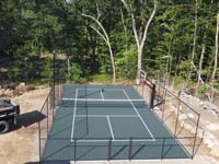 Lenthwise low drone view of green court in Lincoln, RI, featuring pickleball with a side of basketball, optional fencing and lighting.