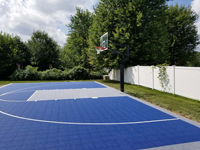 More complete side view, including net, of home basketball court in royal blue and grey tile surface in North Attleboro, MA.