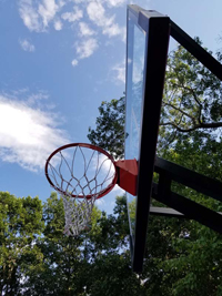 Light blue, red, and royal blue residential basketball court in North Attleboro, MA, showing closeup of hoop from below.