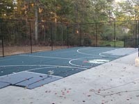 Partial view of court underconstruction in Raynham, MA, with fence and hoops in, and about haalf of sport surface installed.