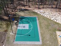 Green and silver court claiming its plan in a Reading, MA yard, seen the long way from overhead. Featuring basketball with lines for pickleball, and high lighting for night play.