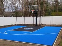 Blue and black backyard basketball court with custom logo and backstop fence in South Yarmouth, MA.