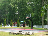 Distance view from direction of front right corner of completed basketball court with a man using it in Taunton, MA.