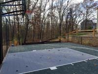 Graphite and titanium residential backyard basketball court in Westford, MA, with retaining wall, gated containment fence, and wood rail fence.