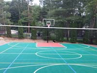 Commercial size multicourt, centered on basketball but with net and lines for volleyball and tennis, installed in a residential backyard in Pembroke, MA, along with an in-ground trampoline and lighting system for night play.