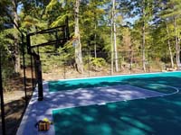 Side view of goal system in end zone of large emerald green and titanium backyard basketball court in Bolton, MA.