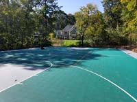 Long view of bulk of large emerald green and titanium backyard basketball court in Bolton, MA, with orange secondary sport lines visible in center court area.