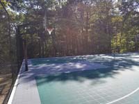 Sunny side view of goal end of large emerald green and titanium backyard basketball court in Bolton, MA.