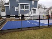 Blue and grey small backyard basketball court with custom red H logo in Braintree, MA, before finishing landscape and hardscape touches.