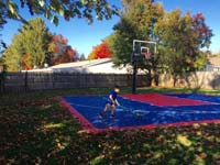 Boy sweeping leaves off navy blue and red backyard basketball court in Canton, MA.