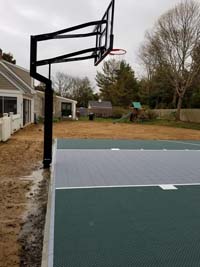 Side view of freshly installed dark green basketball court and hoop, ready for fresh landscaping around it, in Duxbury, MA.