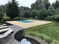 Small backyard basketball in Easton, MA, tiled in sand color, with green key. Shown after landscaping was done and fun is obviously being had by players of all ages.