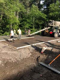 Concrete being pored and smoothed for base of what will become a blue and gray residential basketball court in Easton, MA.