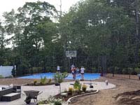 Kids shown on blue and gray residential basketball court in Easton, MA, with landscaping by Evergreen still in progress in foreground.