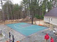 Green and black basketball court in Marion, MA, shown before completion of surrounding landscaping and pool.