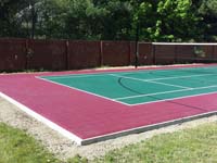 A view of most of backyard basketball court in Sudbury, MA, emphasizing tennis net in background and the quality concrete base under court tiles in foreground.