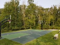 Left front angled overview of backyard basketball court in shades of green, set in finished landscape with stone benches, in Dartmouth, MA.