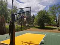 Olive green and yellow basketball court in Easton, MA, featuring lighting extension on goal system for night play.