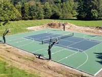Low level aerial view at an angle down the long axis of a substantial combined basketball and tennis court in Easton, MA.