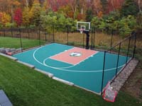 Low drone view of a green backyard basketball court in completed landscape in Middleton, MA with backdrop of fall colors.