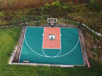 Drone view straight down at green and rust custom basketball court in a yard in Middleton, MA.