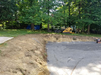 Back left end of excavated and leveled site with stone dust underlay in prep for monochrome blue hilltop home basketball court in Milton, MA.