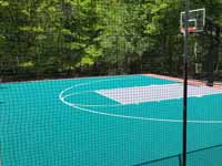 Residential backyard basketball court on fresh concrete base in stalled in Pepperell, MA, featuring fencing and an emerald green, titanium, and rust red sport tile surface.