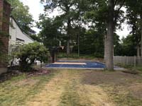 Ground level view of side of blue and peach or salmon basketball and pickleball court at ground level from across backyward in Randolph, MA.