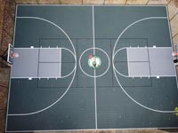 Aerial view of large backyard basketball court in Raynham, MA, with drak green and silver tiles and a custom Celtics logo.