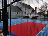 View through optional mesh fence from behind court adjacent to hoop, across red key toward house in Shirley, MA.