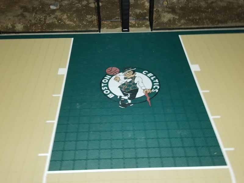 Photo from installation of a sand and emerald green residential backyard basketball court in Swampscott, MA. Looking down at court from ladder while adjusting lighting system.