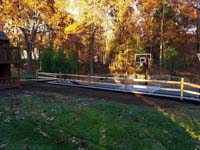 Graphite and titanium residential backyard basketball court in Westford, MA, with retaining wall, gated containment fence, and wood rail fence.