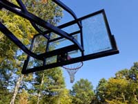 Skyview from beneath hoop at one end of large emerald green and titanium backyard basketball court in Bolton, MA.