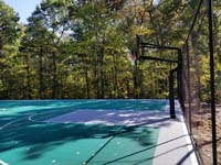 Side view of most of hoop and key end of large emerald green and titanium backyard basketball court in Bolton, MA.