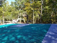 View of one end of large emerald green and titanium backyard basketball court in Bolton, MA.