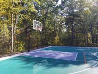 Focus on end zone, showing off fence and goal, of large emerald green and titanium backyard basketball court in Bolton, MA.