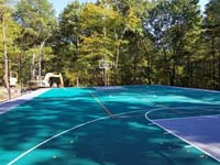 Long view of most of large emerald green and titanium backyard basketball court in Bolton, MA.