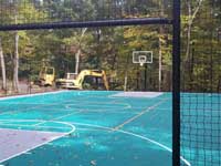 View through gateway in fence around large emerald green and titanium backyard basketball court in Bolton, MA.