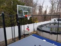 Corner detail of blue and grey basketball court in Braintree, MA, highlighting hoop and tall rebound fence.