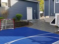 View of entry corner of blue and grey basketball court in Braintree, MA, showing hockey net and associated patio.