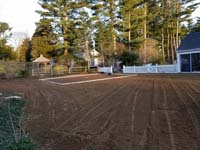 Prep work for construction of dark green basketball court in Duxbury, MA, in context of owner's wider backyard landscaping.