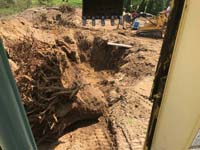 Stump removal and excavation in preparation to install a tan and green basketball court in Londonderry, NH, featuring multiple custom logos and writing, lighting for night play, and optional multicourt net for volleyball.