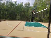 Tan and green basketball court in Londonderry, NH, featuring multiple custom logos and writing, lighting for night play, and optional multicourt net for volleyball.