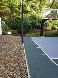 Context and portion of slate green and titanium small home basketball court in Needham, MA.