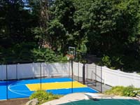 Royal blue and yellow basketball court and accessories in Stoneham, MA, viewed from adjacent covered pool.