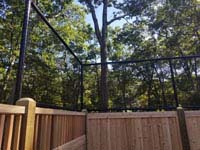 Corner view of custom fence solution combining cedar wood fence and more traditional rebounder/containment fencing in reduced height to top it. This goes with graphite and orange residential basketball court in Walpole, MA.